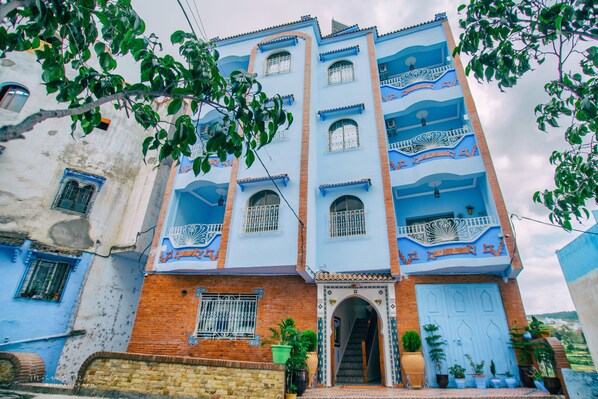 A multi-story building with a blue facade, multiple balconies, and a central entrance with a staircase.