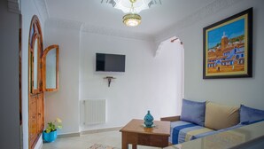A living room with a sofa, a television mounted on the wall, a wooden cabinet, and a painting. - Dar Jinane 2: Cosy and Stylish (Chefchaouen)