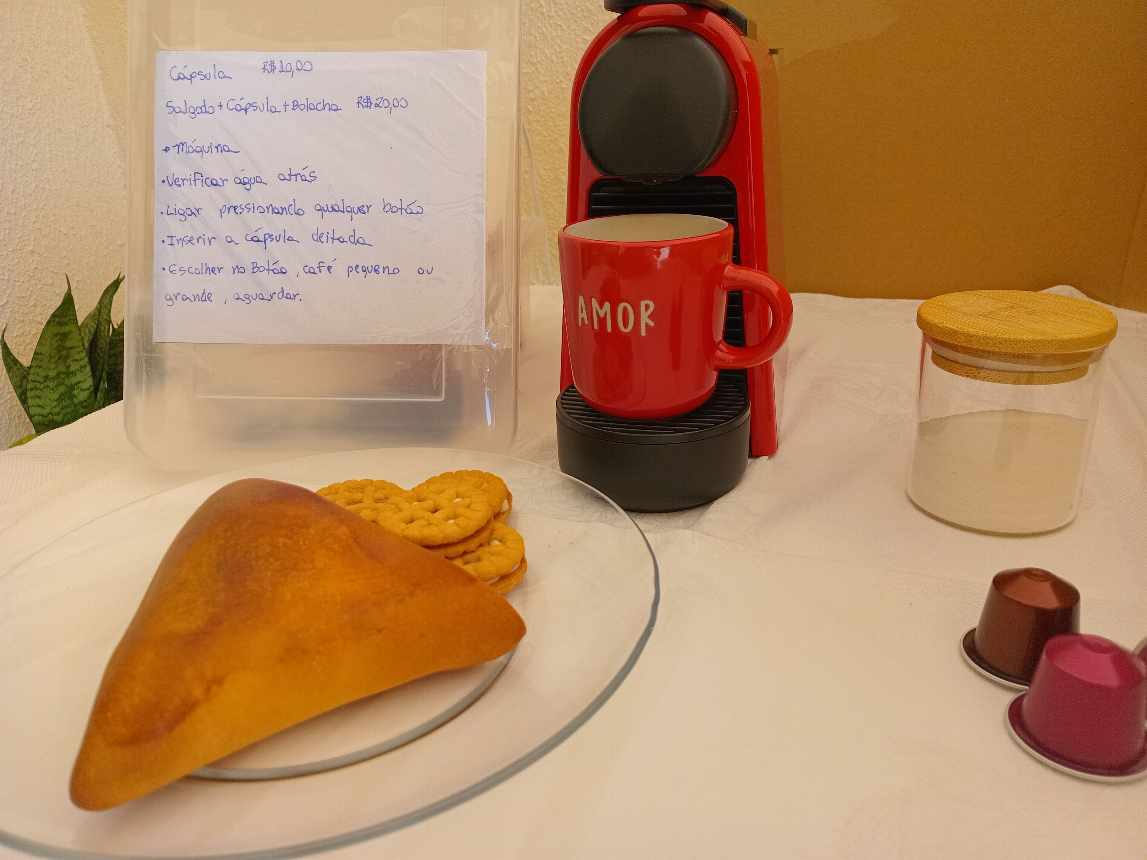 A table with a red coffee maker, a glass jar, a red mug, and a plate with a pastry and cookies.