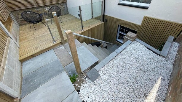 A modern outdoor area with a wooden deck, a seating area with chairs, and a stone staircase leading to a higher level. - Hideaway 1-bed Apartment in Herne Bay (Herne Bay)