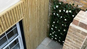 A small outdoor area with a wooden fence, a window, and a brick wall. - Hideaway 1-bed Apartment in Herne Bay (Herne Bay)