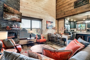 A cozy living room with a fireplace, comfortable seating, a dining area, and a kitchen.