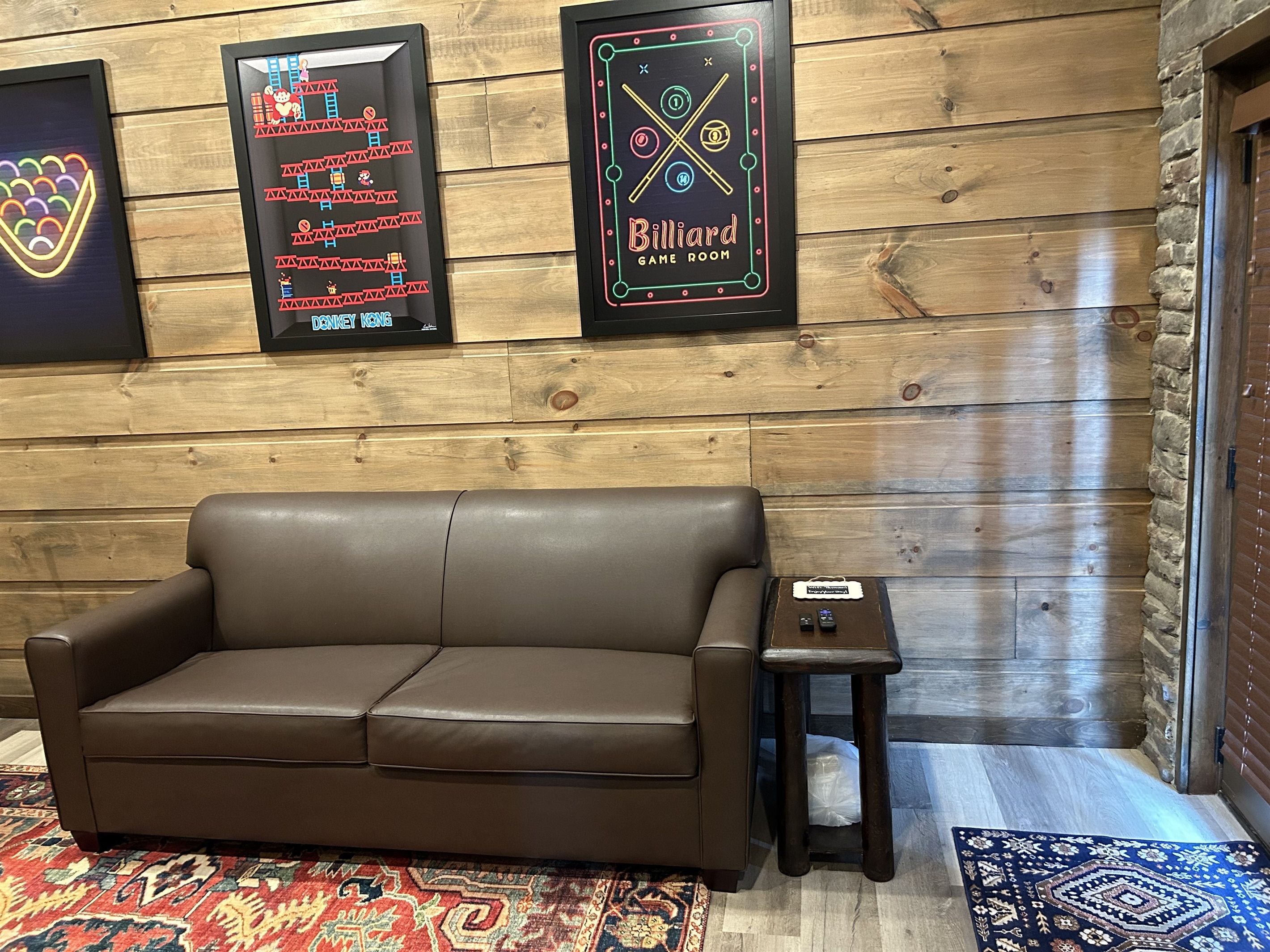 A brown leather sofa, a small side table, and a billiard game room sign on a wooden wall.