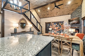 Una cocina moderna con encimeras de granito, una zona de comedor con una mesa y sillas de madera, y una escalera que sube a un nivel superior.