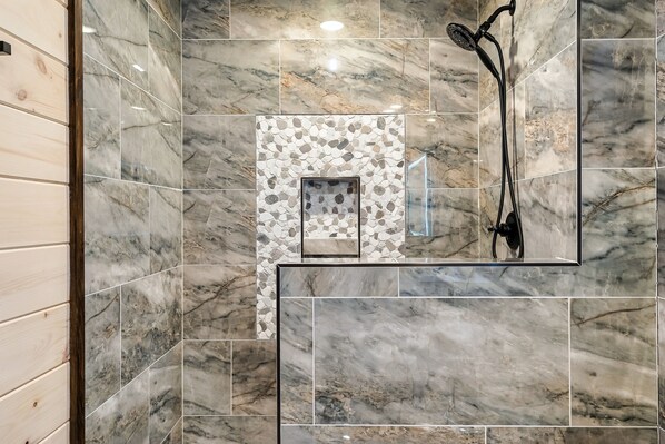 Un baño con baldosas de mármol, una zona de ducha y un panel de madera a la izquierda.