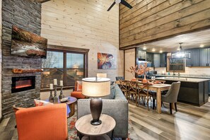 Amplia sala de estar con chimenea, una mesa de comedor y una cocina al fondo.