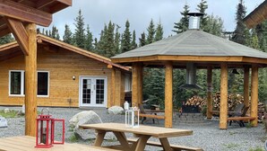 Eine Holzhütte mit überdachter Außenbereich, Picknicktischen und einem Feuerkorb.