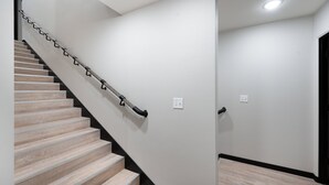 A staircase with wooden steps and a metal handrail, leading to a landing with a white wall and a light switch.