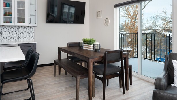 A modern kitchen with white cabinets, a dining table with chairs, and a large window with a view of a backyard.