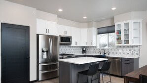 A modern kitchen with stainless steel appliances, white cabinetry, and a central island with bar stools.