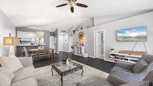 A spacious living area with a ceiling fan, a dining area, a kitchen, and a TV mounted on the wall.