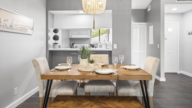 A dining area with a wooden table set for four, a chandelier, and a kitchen in the background.