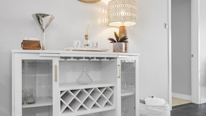 A white console table with a glass wine rack, a decorative lamp, and a small plant.