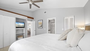 A bedroom with a large bed, white walls, a ceiling fan, and built-in closets.