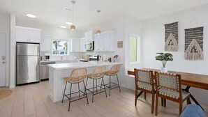Una cocina moderna con armarios blancos, un refrigerador de acero inoxidable y una isla central con taburetes de bar.