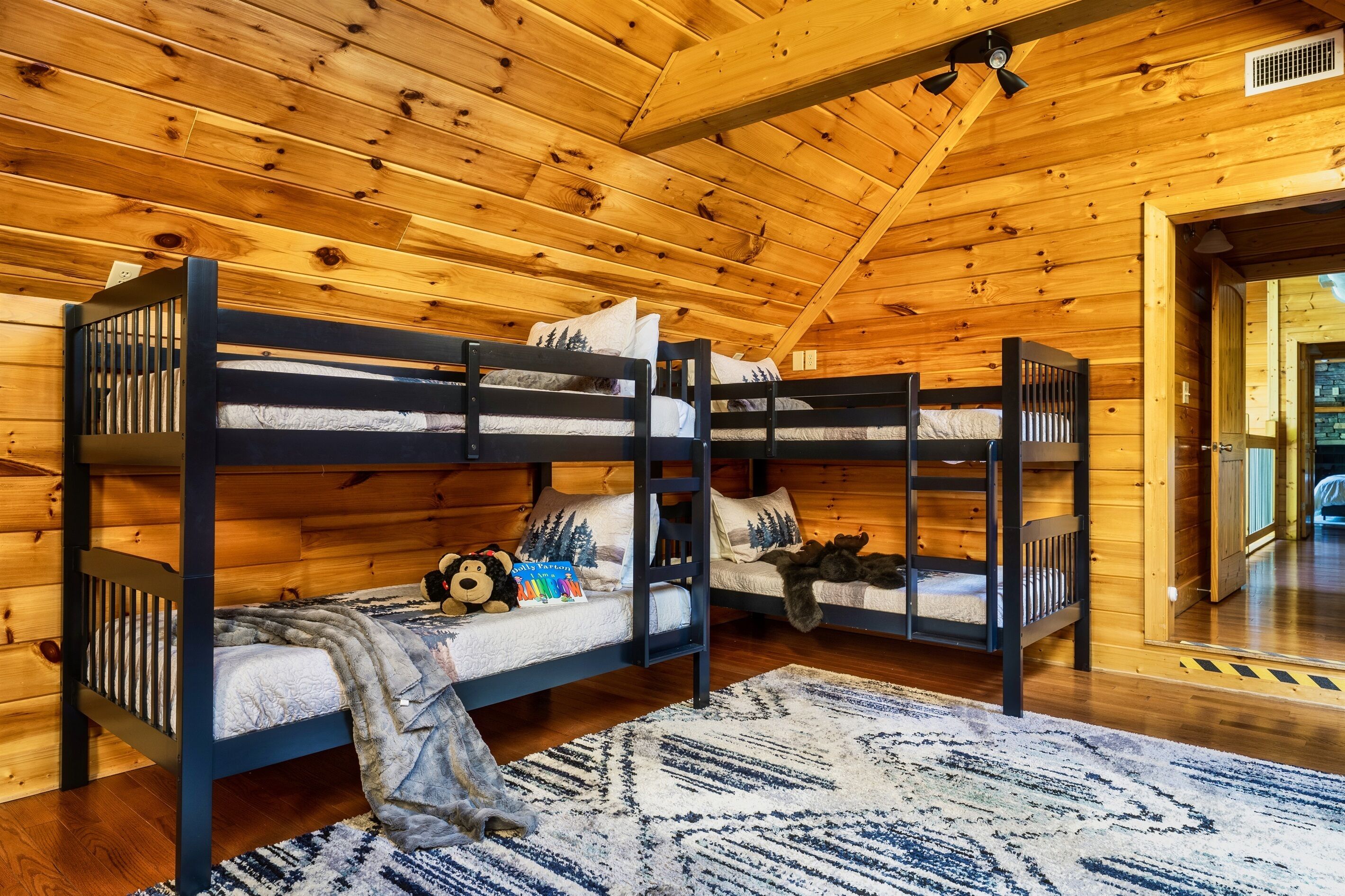 Eine Holzhütte mit drei Etagenbetten, Holzwänden, einem gemusterten Teppich und einem Deckenventilator.