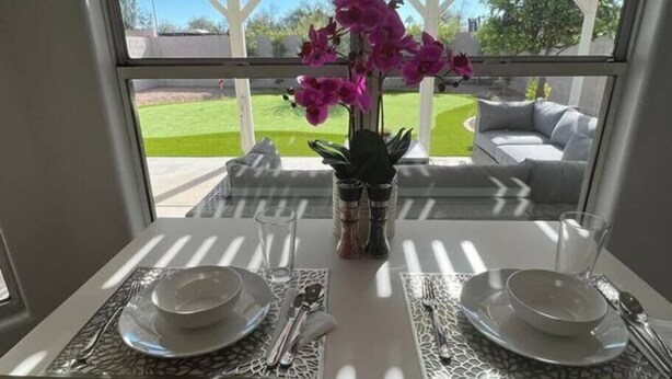 A dining table set with plates, cutlery, and glasses, with a window view of a lawn and a white structure.