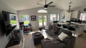A modern living room with a grey sofa, a dining area, and a kitchen.