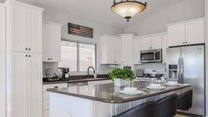 A modern kitchen with white cabinets, a central island with bar stools, stainless steel appliances, and a decorative plant.