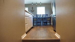 Un couloir étroit au plancher de bois, un coin repas avec deux chaises et un réfrigérateur.