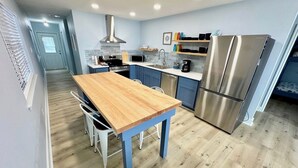 A modern kitchen with a wooden table, blue cabinets, stainless steel appliances, and a view into the living area. - WATERFRONT Burnett House Up (Port O'Connor)