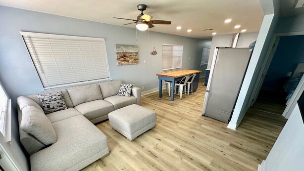 A modern living room with a grey sectional sofa, a wooden dining table, and a ceiling fan. - WATERFRONT Burnett House Up (Port O'Connor)