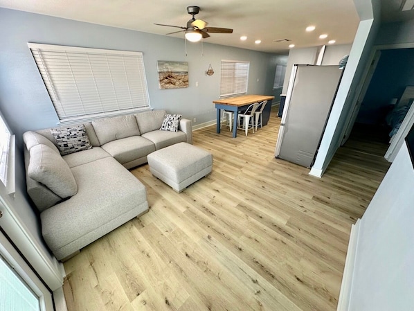 A modern living room with a grey sectional sofa, a wooden dining table, and a ceiling fan. - WATERFRONT Burnett House Up (Port O'Connor)
