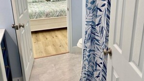 A bedroom with a bed, a ceiling fan, and a bathroom visible through an open door. - WATERFRONT Burnett House Up (Port O'Connor)