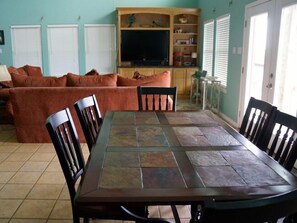 Un coin repas avec une table et des chaises, un canapé et un téléviseur en arrière-plan.