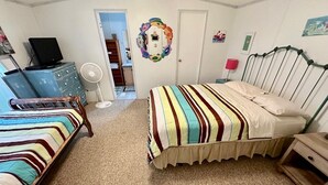 Een slaapkamer met twee bedden, een dressoir, een ventilator en een deur naar een andere kamer.