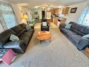 A living room with two dark sofas, a wooden coffee table, and a kitchen in the background.