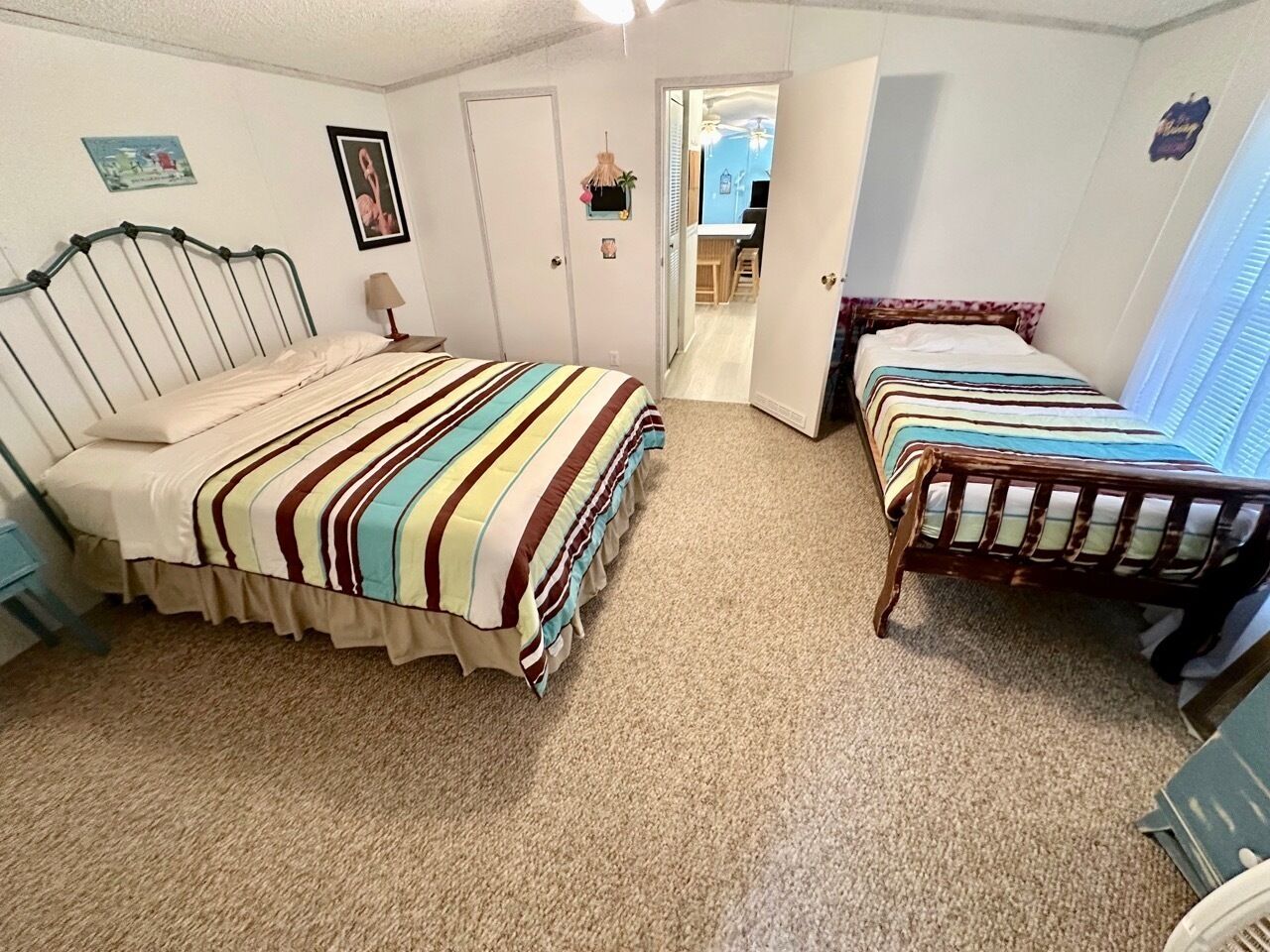 A bedroom with two beds, a door leading to a bathroom, and a small desk with a chair.