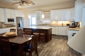 Una cocina moderna con armarios blancos, una isla central con taburetes, una mesa de comedor con sillas y un ventilador de techo.