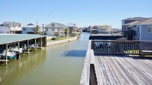 Una propiedad frente al agua con un muelle de madera, zona cubierta para embarcar barcos y edificios residenciales a lo largo de la orilla.