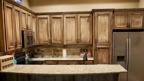 Una cocina con armarios de madera, encimera de granito, refrigerador de acero inoxidable y una barra con taburetes.