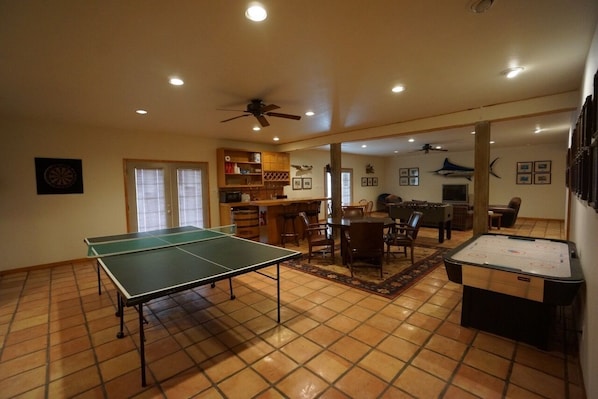 Amplia sala de estar con mesa de ping pong, mesa de fútbol y comedor con sillas y una mesa.