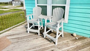 A turquoise house with a wooden deck, two Adirondack chairs, and a window with blinds. - PARKERSON HOUSE in Larry's Harbor POC (Port O'Connor)
