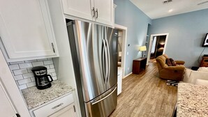 A modern kitchen with white cabinets, a stainless steel refrigerator, a coffee maker, and a wooden floor. - PARKERSON HOUSE in Larry's Harbor POC (Port O'Connor)
