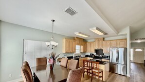 Una cocina moderna con armarios de madera, un refrigerador de acero inoxidable y un comedor con mesa de madera oscura y sillas estampadas.