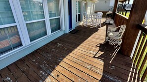 Un porche cubierto con piso de madera, muebles de exterior blancos y ventanas grandes.
