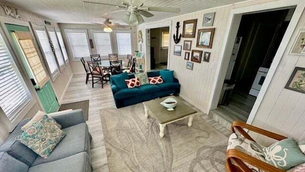 A spacious living room with a blue sofa, a wooden coffee table, and a patterned rug. There is a dining area with chairs and a table, and a ceiling fan. - SIREN COVE is Close to Beach in POC (Port O'Connor)