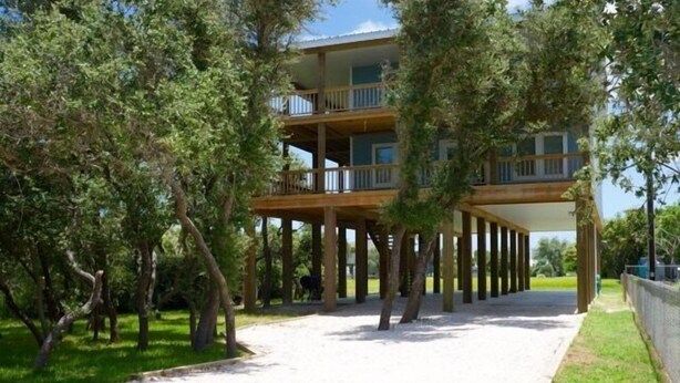 A multi-story building with balconies, supported by wooden pillars, surrounded by trees. - TEXAS TREEHOUSE is Close to Beach in POC (Port O'Connor)