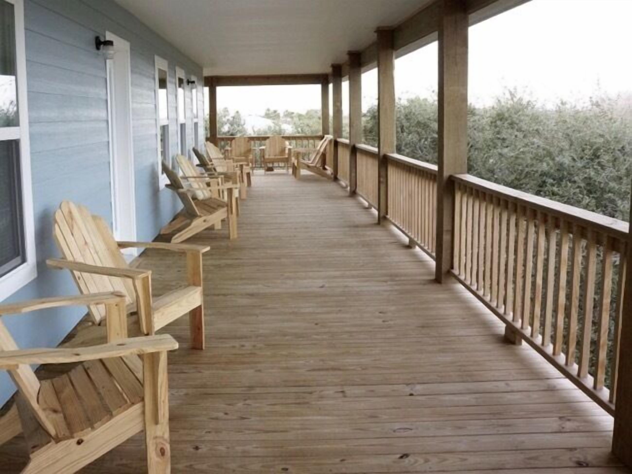 A covered wooden deck with rows of wooden chairs facing a building with large windows.