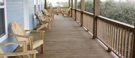 A covered wooden deck with rows of wooden chairs facing a building with large windows.