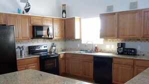 A kitchen with wooden cabinets, a granite countertop, a black refrigerator, a stove, a dishwasher, a microwave, and a coffee maker. - TEXAS TREEHOUSE is Close to Beach in POC (Port O'Connor)
