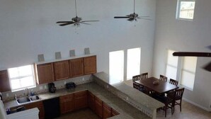 A kitchen with wooden cabinets, a granite countertop, a dining table with chairs, and two ceiling fans. - TEXAS TREEHOUSE is Close to Beach in POC (Port O'Connor)