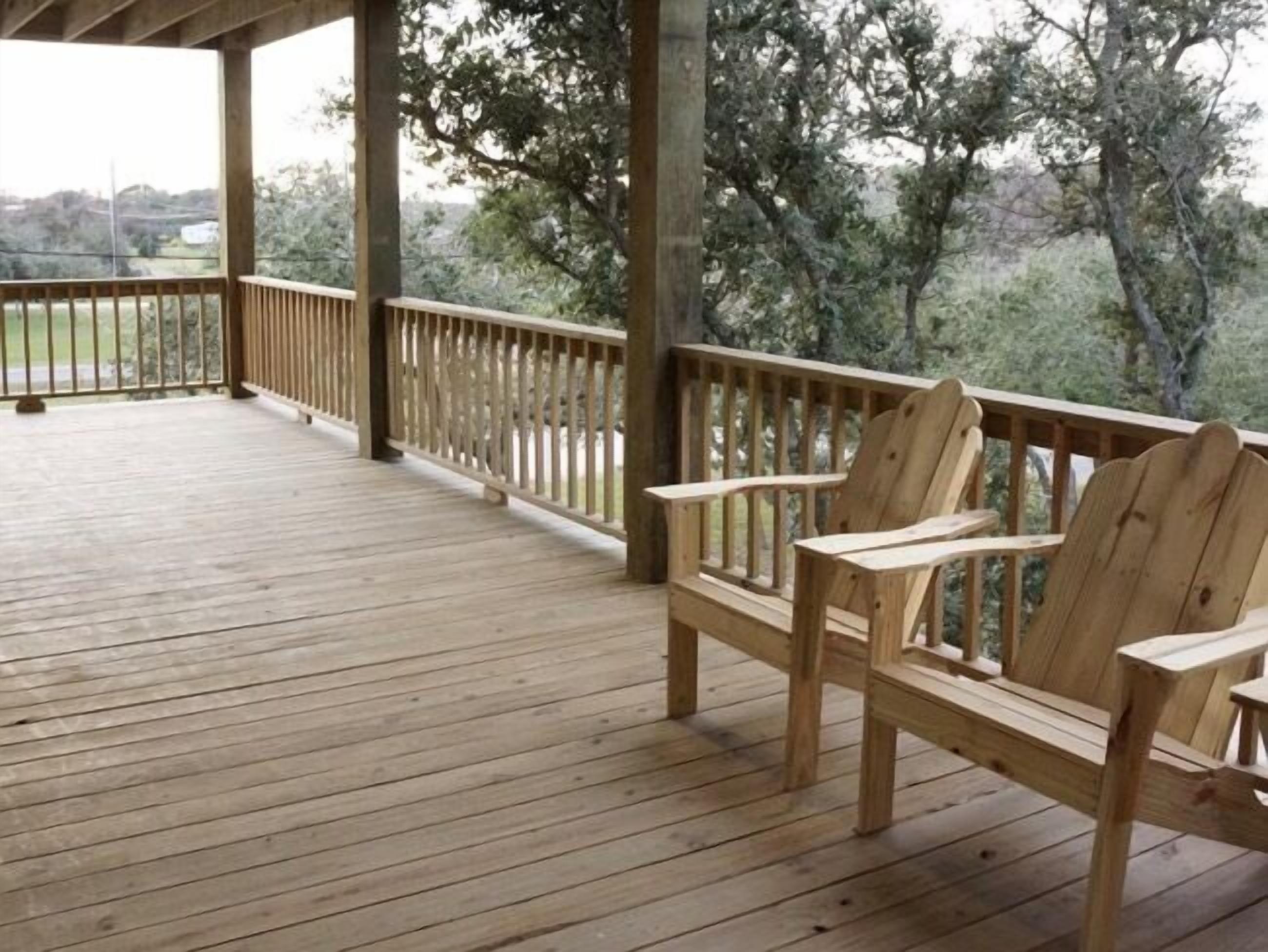 Une terrasse en bois avec un banc, entourée d’arbres et d’une clôture.