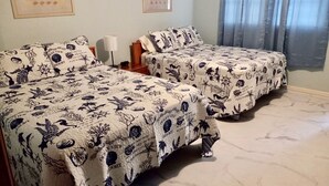 Due letti con lenzuola a tema marino coordinato, un comodino con una lampada e un quadro appeso al muro.