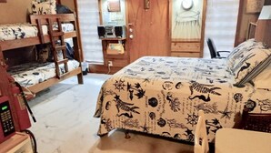 A room with a bunk bed, a desk with a computer, a chair, and a bed with a nautical-themed bedspread.