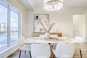A dining area with a large window, a chandelier, and a modern abstract painting. - Skyline Suites - Next to MTCC, ACC & CN Tower (Toronto)